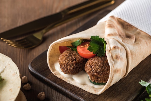 Close up view of falafel with vegetables and sauce in pita on wooden table