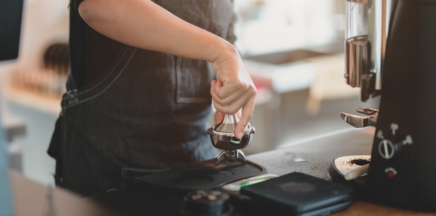 Vista del primo piano del caffè stridente della mano femminile di barista con la macchina della smerigliatrice