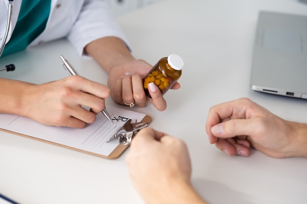 Close up view of female doctor hand holding bottle with pills and writing prescription