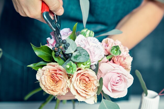 ショップで新鮮な花の花束を作る女性の花屋のビューを閉じます。女性は装飾やアレンジをするために束を切りました。コピースペース。プロの花屋のコンセプト