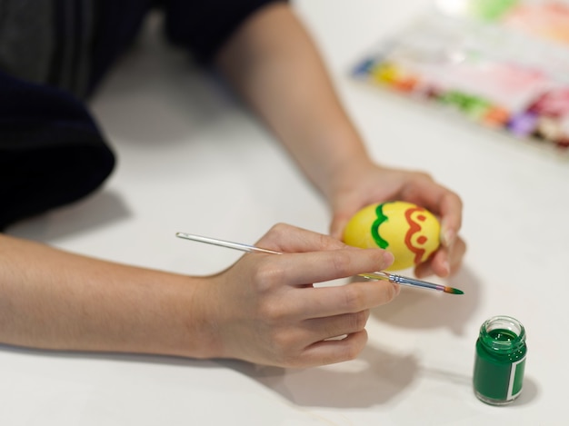 Vista ravvicinata delle mani femminili che dipingono sulle uova per preparare per la festa di pasqua sulla tavola del mestiere