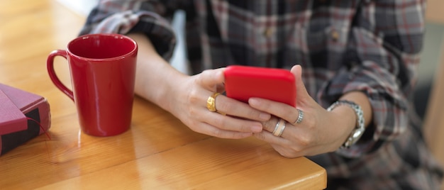 Close up view of female hands using smartphone on wooden table with coffee mug