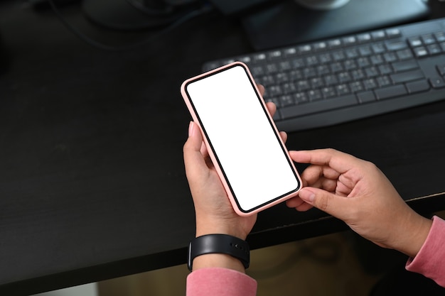 Vista ravvicinata della femmina tenendo il telefono cellulare con lo schermo vuoto nel suo posto di lavoro. schermo vuoto per il montaggio del display grafico.