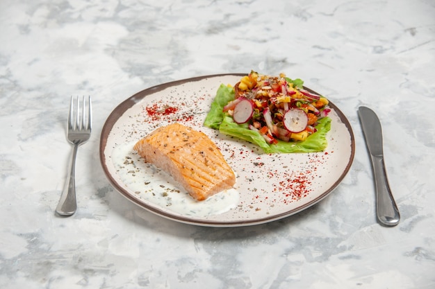 Close up view of fish meal and delicious salad on a plate and cutlery set on stained white surface with free space