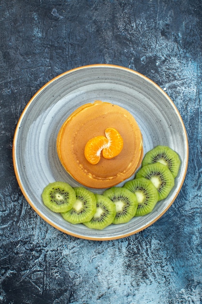 Close up view of fluffy American-style pancakes made with natural yogurt served with kiwifruit and tangerine on a plate on ice background with free space