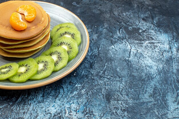 Close up view of fluffy American-style pancakes made with natural yogurt served with kiwifruit and tangerine on a plate on the right side on ice background