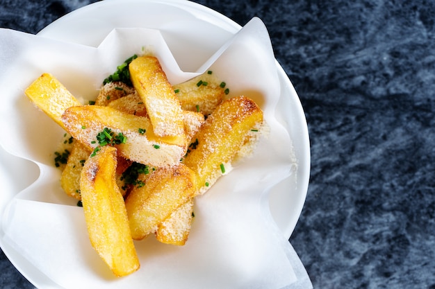 Close up view on French fries with sauce, garlic and cheese in craft paper. Fast food, snack.