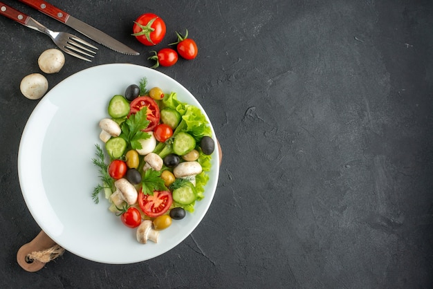 Vista ravvicinata di verdure fresche tritate di olive nere e gialle su un piatto bianco e posate su sfondo nero con spazio libero Foto Premium