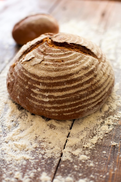 Close up view of fresh brown crispy loaf of bread lying on the wooden table sprinkled with flour