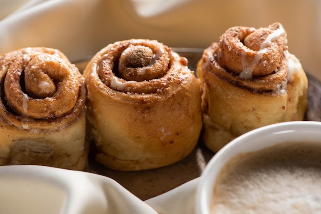 Close up view of fresh homemade cinnamon rolls on board on satin cloth with coffee