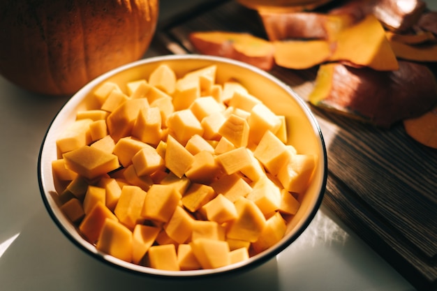 Vista ravvicinata di pezzi di zucca arancione freschi e vividi in un piatto bianco.