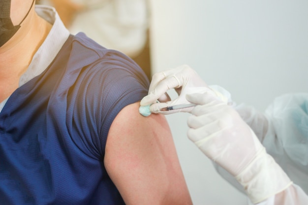 Photo close up view of an getting vaccine shot in his arm during corona virus pandemic. patient in medical mask. covid-19 or coronavirus vaccine