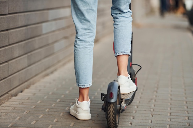 Close up view of girl in casual clothes that riding electric schooter outdoors at sunny daytime