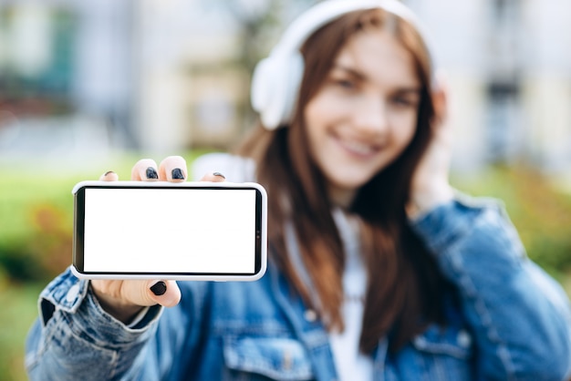 Close-up view of a girl in headphones on a blurred background shows a white phone screen, copy space