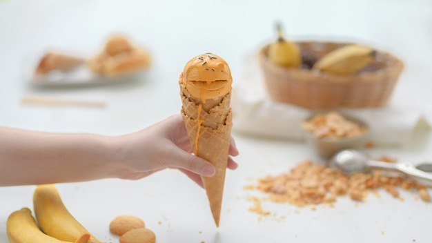 Close up view of a girl holding peanut butter banana ice-cream cone on white table