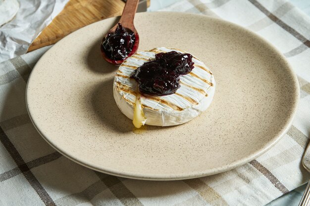 Close up view grilled Camembert cheese head on plate and on cutting board with jam. light texture table.