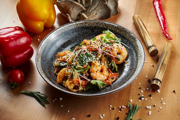 Close up view on Grilled tiger prawns and scallops with pasta udon in a black bowl on a wooden surface