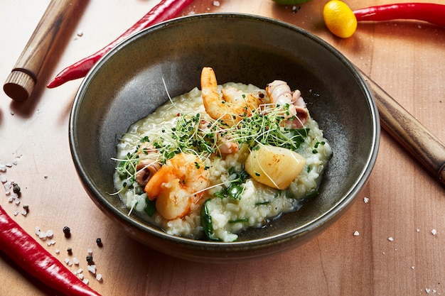 Close up view on Grilled tiger prawns and scallops with risotto in a black bowl on a wooden surface