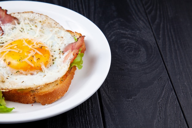 Close up view on grilled toast with bacon and egg on white plate on dark wooden background. Copy space. Food phoro for breakfast. Top view