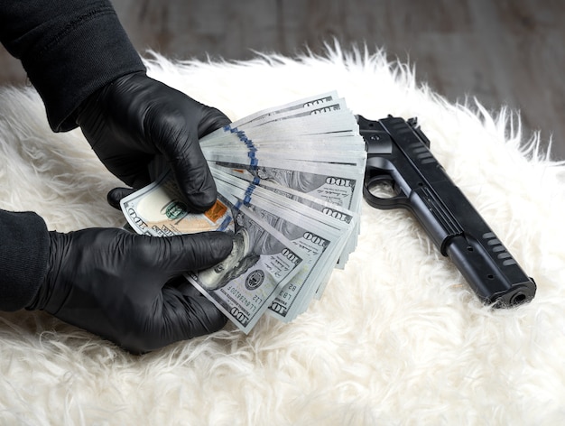 Photo close-up view of gun and dollars in hands of robber in gloves