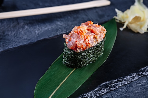 Close up view on gunkan sushi with spicy sauce and tuna on dark stone surface