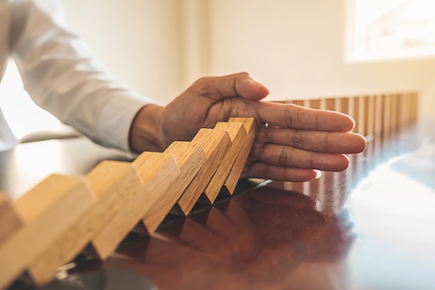 Photo close up view on hand of business woman stopping falling blocks on table.