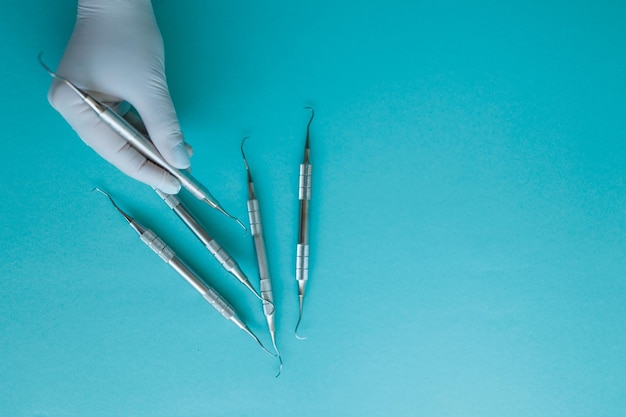 Close up view hand of a dentist in a latex glove taking a periodontal scaler on a blue background