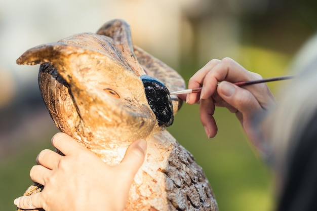 Close up view of the hand of a woman painting a polystyrene owl figurine outdoors