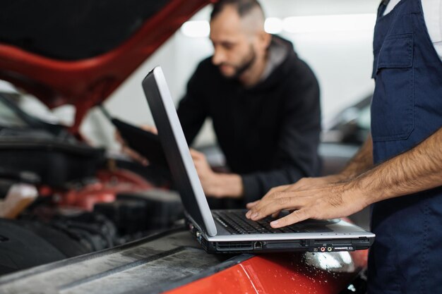 Photo close up view of hand of young male mechanic using laptop and his colleague with tablet