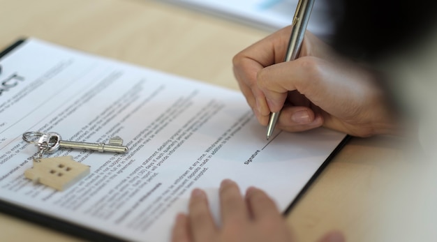 Photo close-up view hands of businessman signing leasing home documents and have a apartment keys on paperwork.