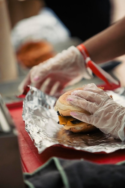 Photo close up view of the hands of a cook preparing a hamburger in a food truck during a music festival.