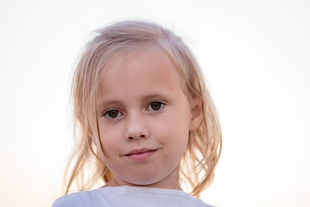 Close up view of little caucasian child girl in white dress posing looking at camera in the summer field at sunset time front view.