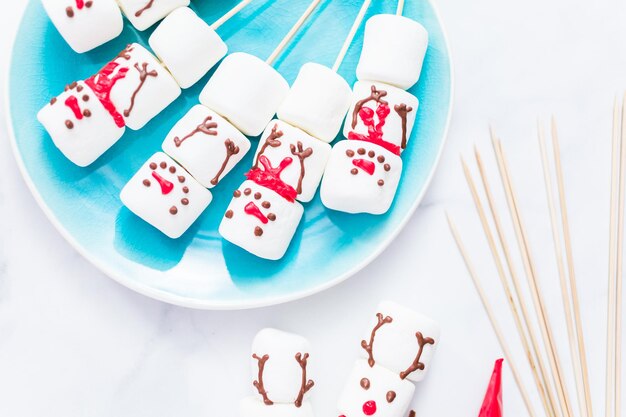 Close up view. Making marshmallow snowman and reindeer on sticks for hot chocolate and cocoa drinks.