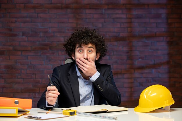 Foto vista ravvicinata ingegnere maschio seduto dietro il suo posto di lavoro in tuta agenda lavoro appaltatore piano di lavoro aziendale business builder