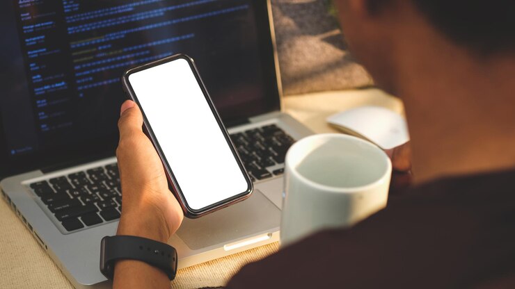 Photo close up view of man drinking coffee and using smart phone at workplace blank screen for your text