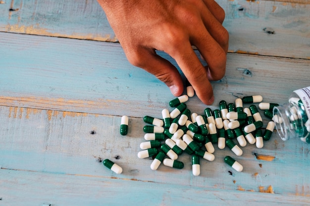 Above close up view of man hand taking medicine pills on a blue wooden table