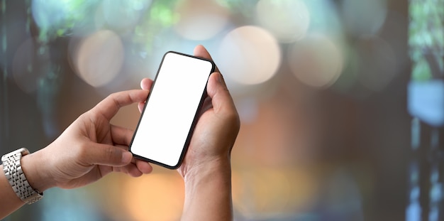 Close-up view of man holding blank screen smartphone with bokeh background