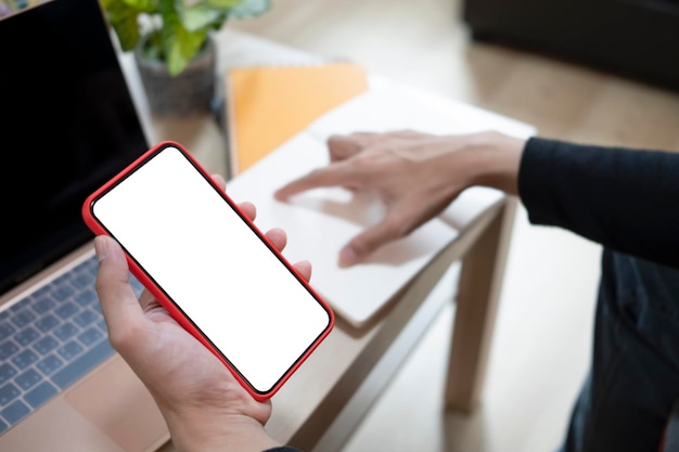 Close up view man holding smart phone and using laptop in living room