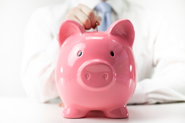 Close up view of man putting coin to pink piggy bank