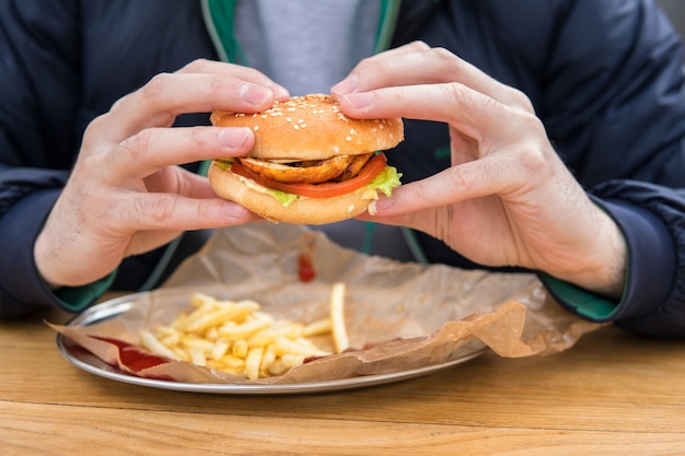 アメリカのハンバーガーで男の手のビューをクローズアップ。ストリートカフェでファーストフードを食べる