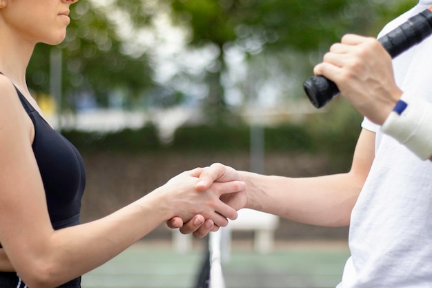 Vista ravvicinata di giocatori di tennis uomo e donna che stringono la mano nel mezzo di un campo da tennis con rete sottostante