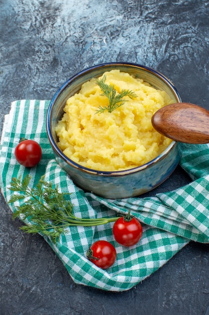 Close up view of mashed potatoes served with dill wooden spoon fresh tomatoes on green stripped towel on dark color background with free space