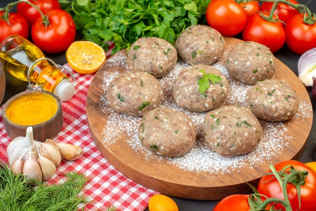 Close up view of meat balls on a brown board and rice flour fresh green lemon fallen oil bottle fresh vegetables yellow ginger on red stripped towel on black background