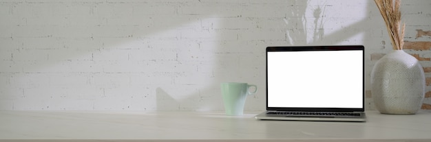 Close up view of minimal workspace with blank screen laptop, mug, decoration and copy space on white table