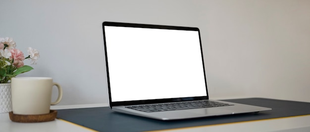 Close up view of mock up computer laptop with empt screen and coffee cup on white table.