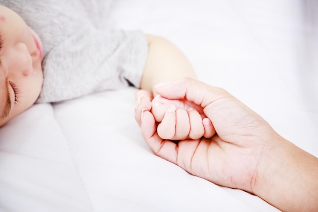 Close up above view of Mother holding hand of her infant on bed Happy family newborn