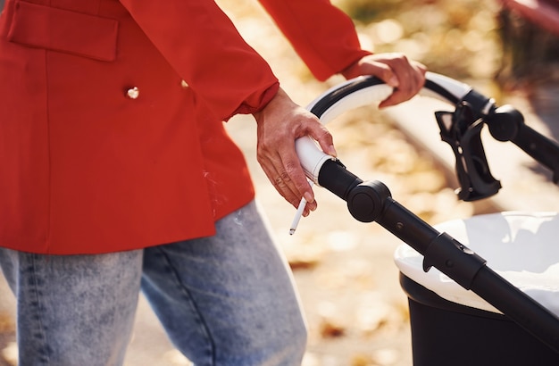 Vista ravvicinata. la madre in cappotto rosso fa una passeggiata con il suo bambino nella carrozzina nel parco in autunno.