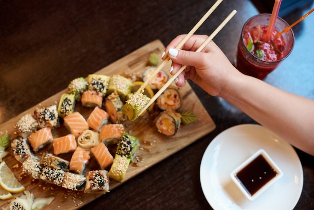 Фото Крупным планом вид вкусных ролл-суши, поданных на деревянной доске с палочками для еды, соевым соусом и коктейлем