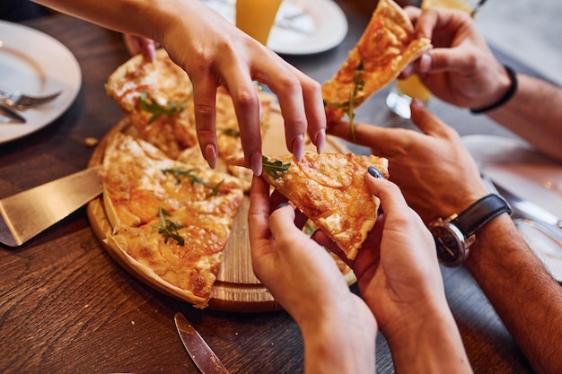 写真 一緒に屋内でピザを食べたり食べたりする人々のクローズアップ。