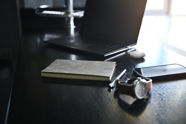 Close-up view of office accessories, laptop, earphones on the box, watch, mobile phone and gray notepad on wooden desk